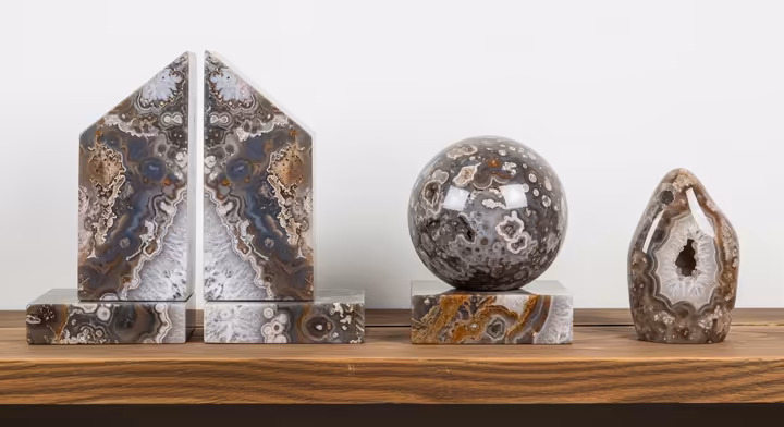 A collection of decorative objects made from Crazy Lace Agate, including polished spheres and bookends, on a wooden shelf.