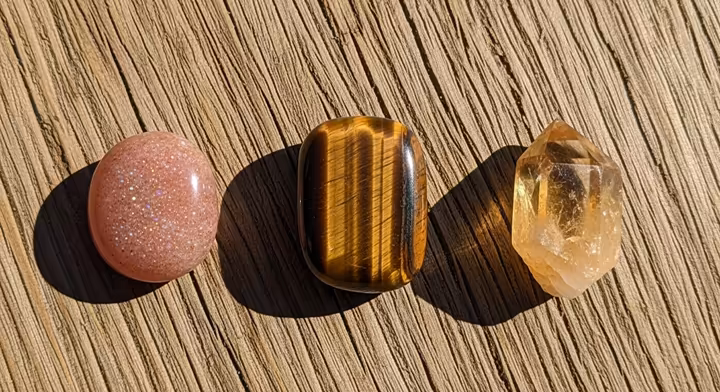 A flat-lay of Sunstone, Tiger's Eye, and Citrine on a rustic wooden background.