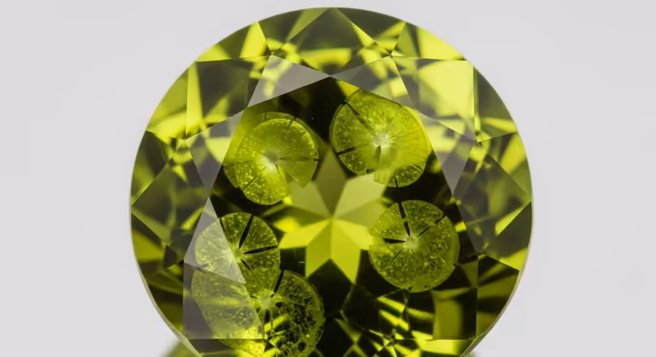 A macro photograph of a brilliant-cut Peridot showing its vibrant lime-green color and double refraction.
